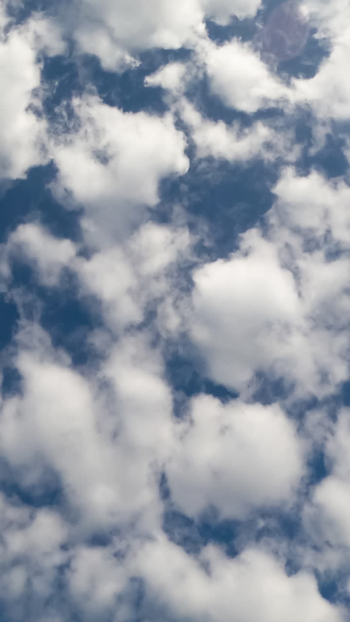 Cumulus clouds in the dark blue sky. Soft white clouds flying in the horizon. Low angle view. Timelapse. Vertical video