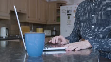 smartly dressed man using the track pad on a laptop on a kitchen counter while working from home with a mug of warm drink next to him close up