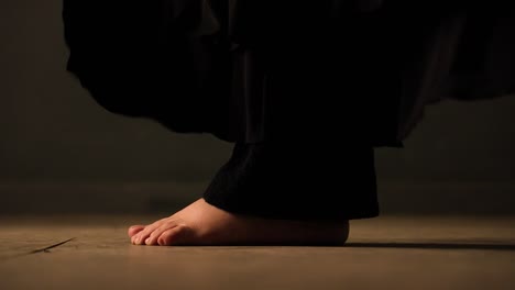 closeup of barefoot feets with black trousers moving, turn, jump and dance on a brown floor