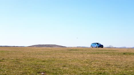 drone capturing aerial footage of a car driving across an expansive field under a clear blue sky
