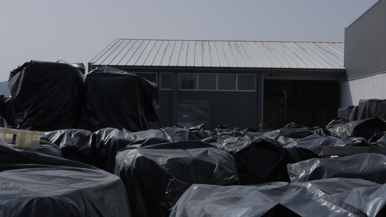 File di grandi sacchi di plastica neri pieni di materiale riciclabile conservati all'esterno di un impianto industriale.
