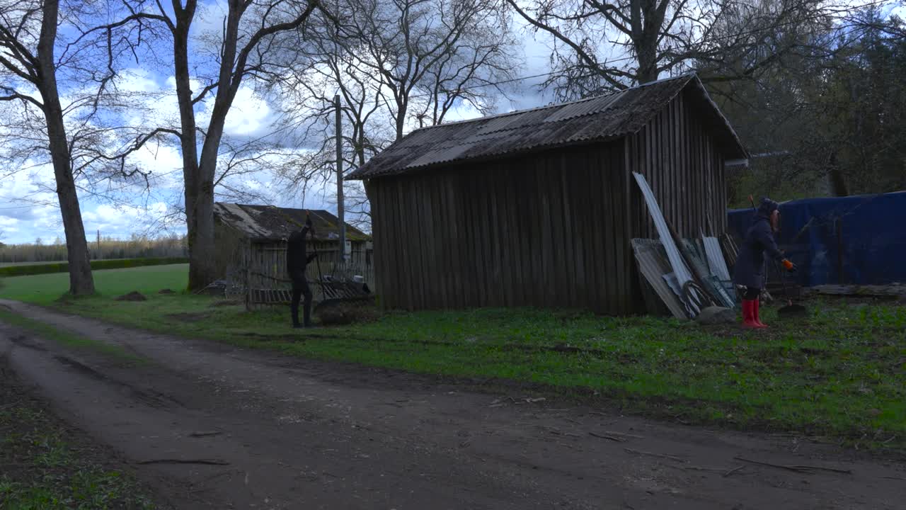 Gorgeous footage of people raking leaves in a sunny garden filmed in timelapse or time lapse mode during summer time or autumn spring. White clouds are moving in the blue sky and green grass visible.