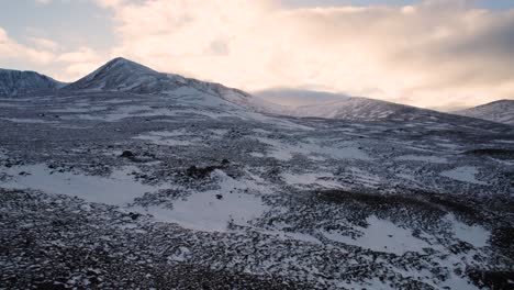 Aerial-drone-footage-slowly-revealing-Fiacaill-Coire-an-t-Sneachda-in-the-Cairngroms-National-Park-in-Scotland-at-sunset-with-a-snow-covered-mountains,-heather-moorland-and-winter-conditions