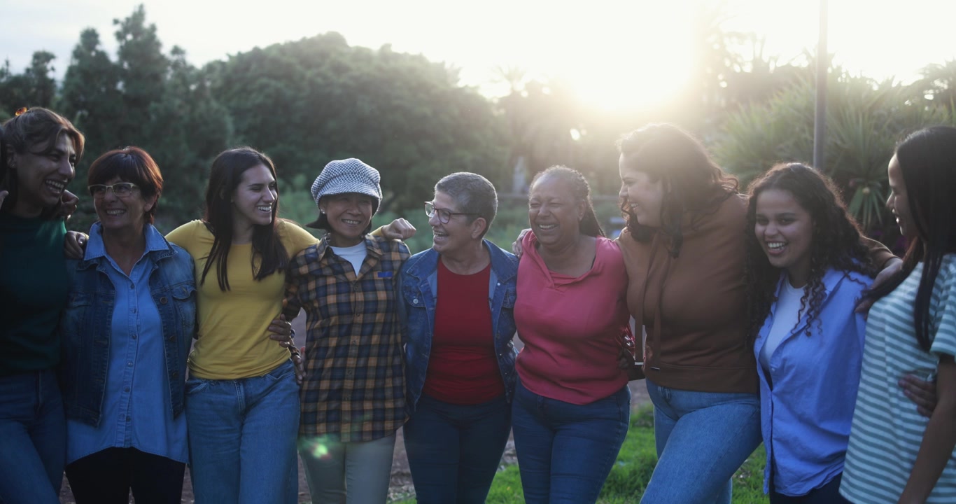 Mujeres diversas y multigeneracionales riendo y abrazándose al aire libre al atardecer