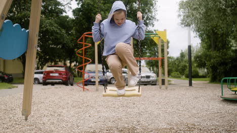 little girl with down syndrome wearing hoodie swinging on a swing in the park on a windy day