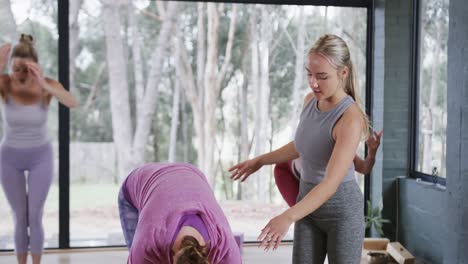 Diverse-female-instructor-guiding-women-with-arms-raised-bending-in-yoga-class