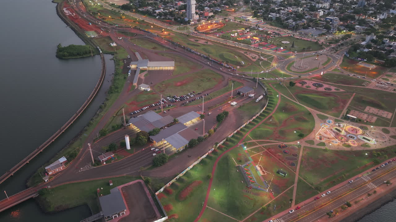 Aerial view of Argentinian urban customs around the green park by the waterfront with a roundabout and walking paths at sunset, Cuarto Tramo, Posadas, Misiones, Argentina.
