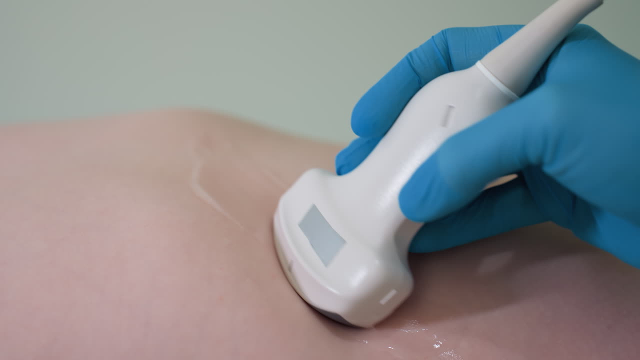 Medical practitioner slowly glides ultrasound probe across young boy's rib area during examination, showing clear detail of diagnostic process with gel trace and gloved hand on smooth skin