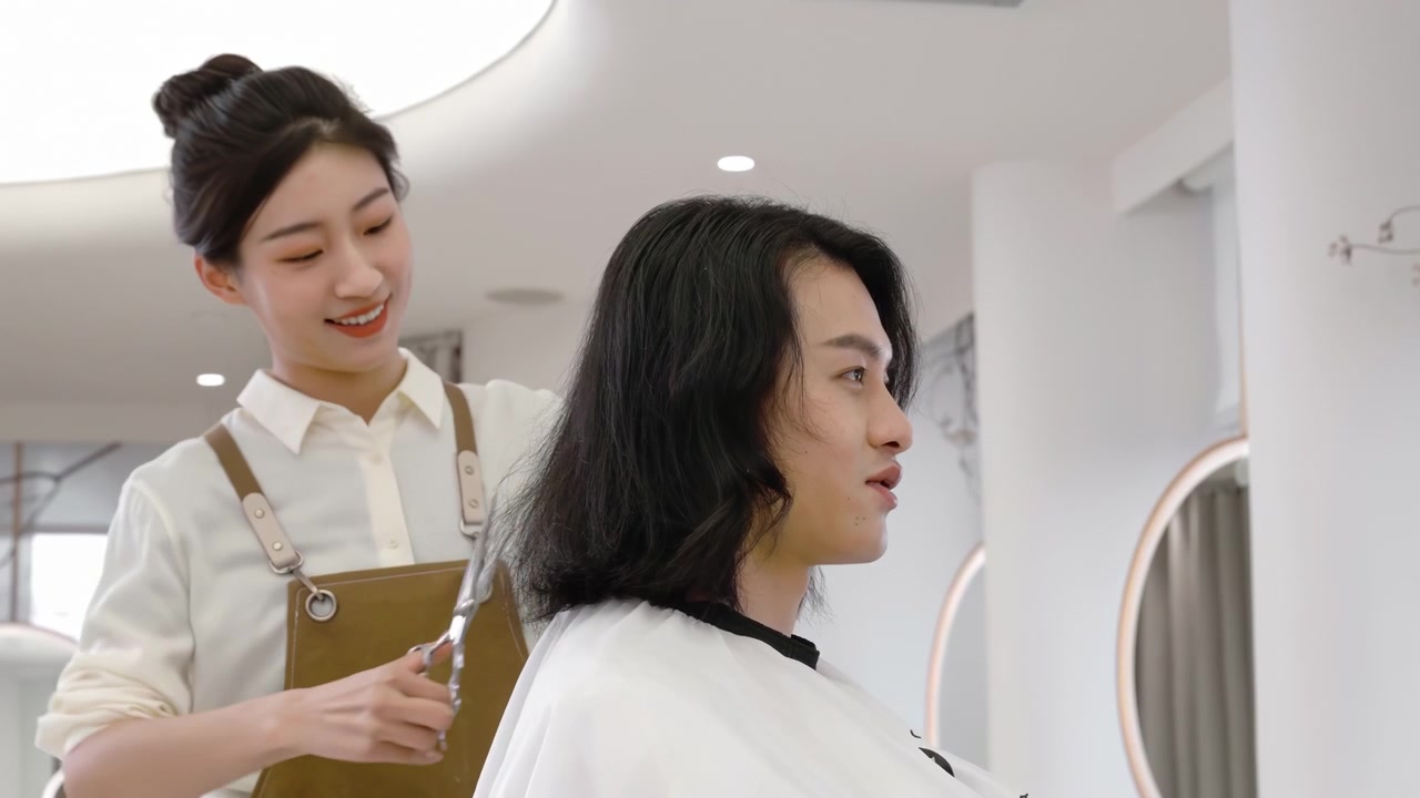 美容室または理髪店で、ヘアスタイリストの女性が男性客とヘア予約前のサービスについて相談し、カット、グルーミング、またはヘアセットを施している様子。