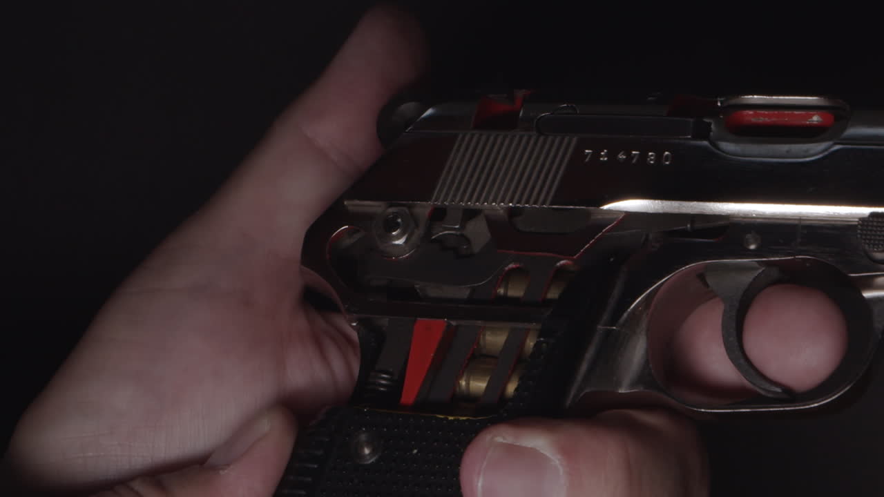 해머가 뒤로 당겨질 때 카트리지를 볼 수 있도록 손잡이가 노출된 권총을 손에 쥐고 있습니다.