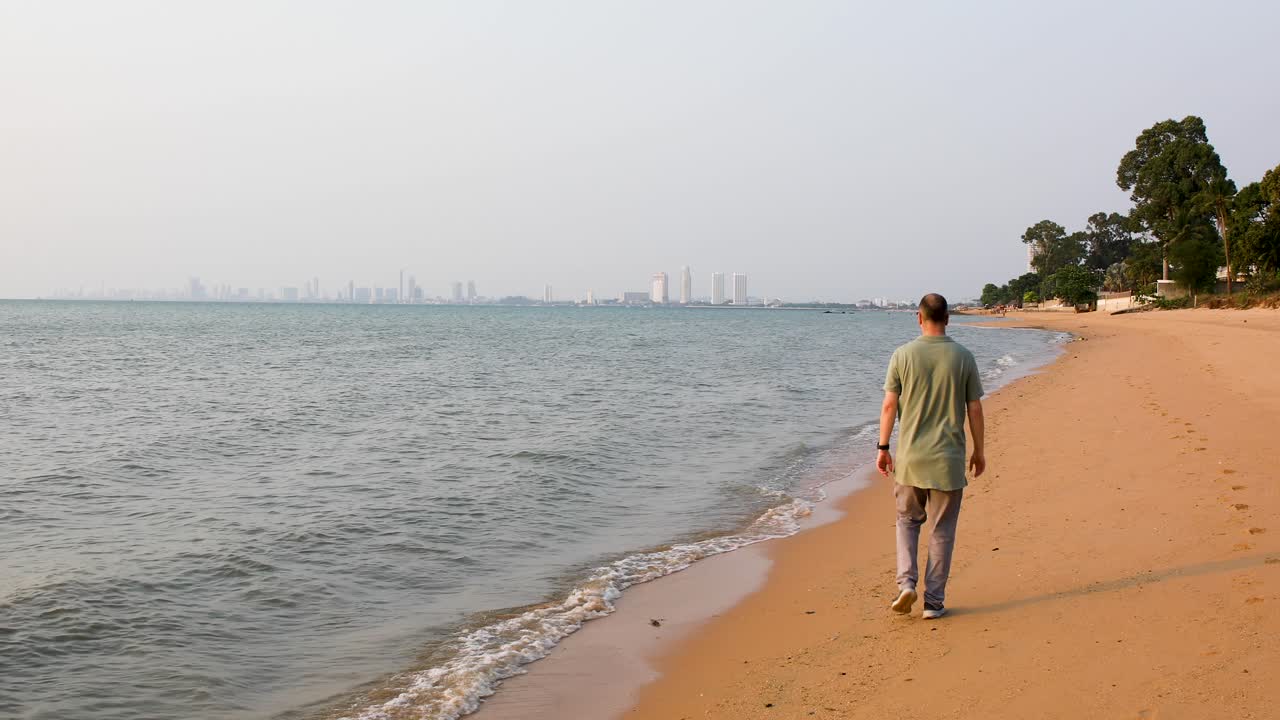 turista masculino caminando por la playa de bangsaray en pattaya, tailandia con vista a la ciudad en la distancia