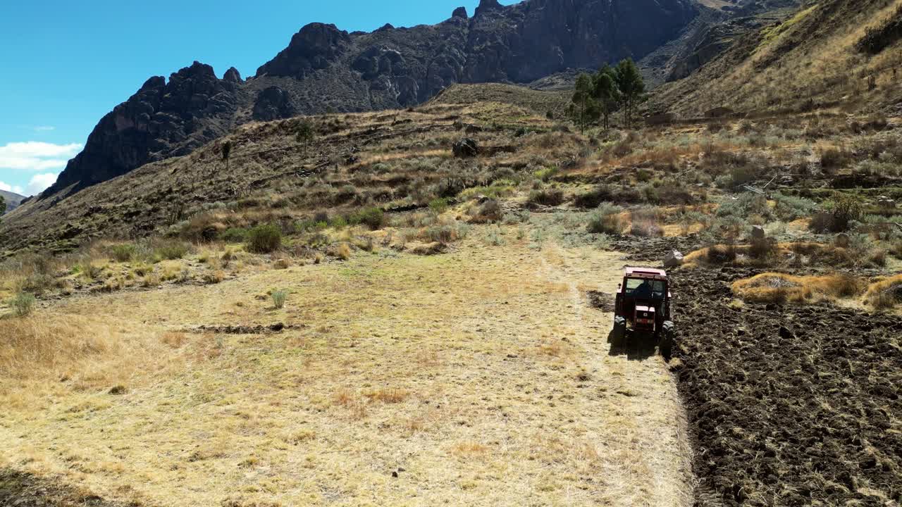 Aerial drone footage of agriculture in the Andes. A red tractor moves methodically across a golden field bordered by stone terraces built by the ancient Inca