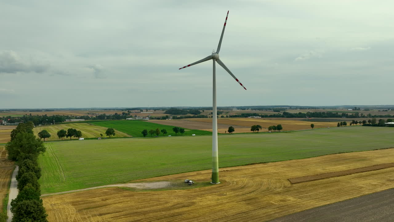 Turbina eolica in un suggestivo paesaggio rurale, circondata da campi con varie sfumature di verde e marrone.