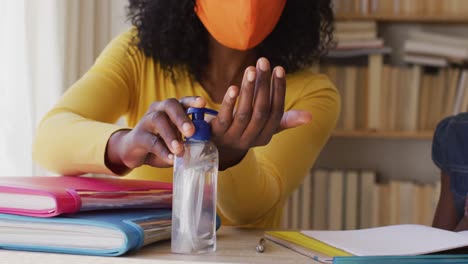 African-american-mother-and-daughter-wearing-face-mask-sanitizing-their-hands-at-home