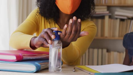 african american mother and daughter wearing face mask sanitizing their hands at home