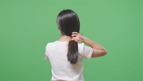 back view of a woman with long black and blond straight healthy hair using her hands making side swept hair in the green screen background studio