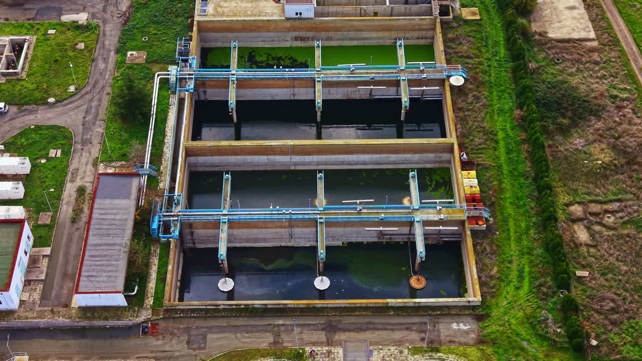 Water treatment facility showcases large pools with green algae and industrial piping under bright daylight in a rural setting