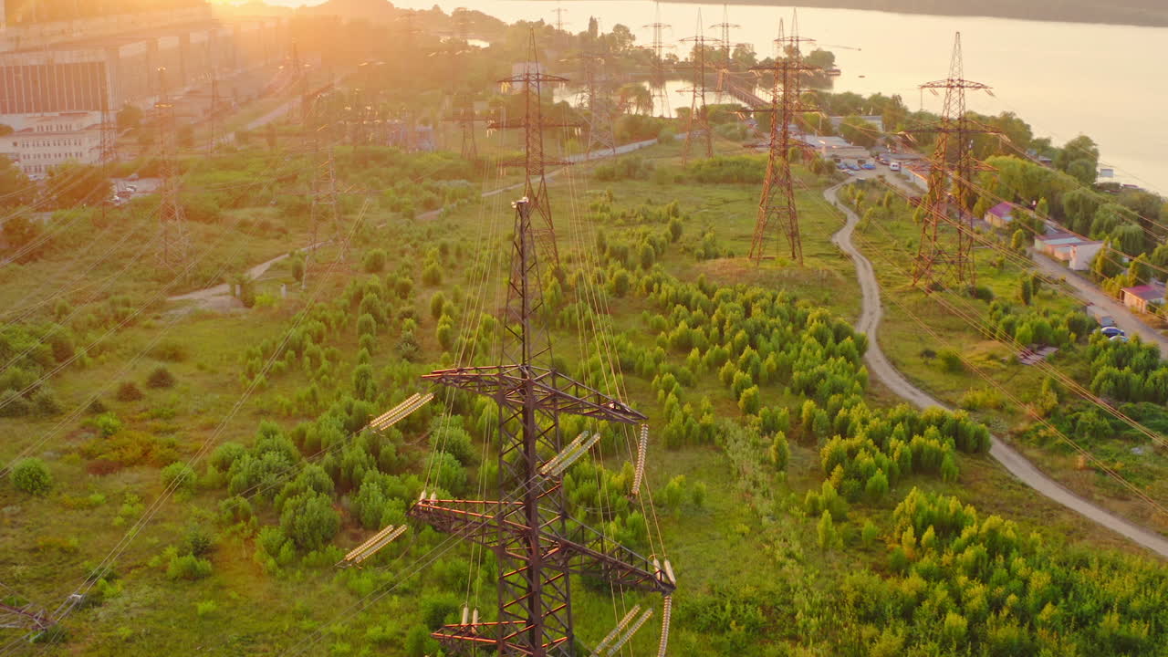 Power line pylons near the river. Electric towers with electric cables with high voltage current. Flight over the transmission lines in the evening. Aerial view.
