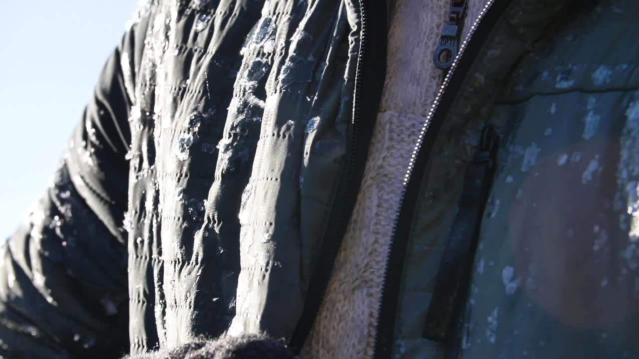 joven viajero desabrochando su chaqueta congelada a la luz del sol a cámara lenta