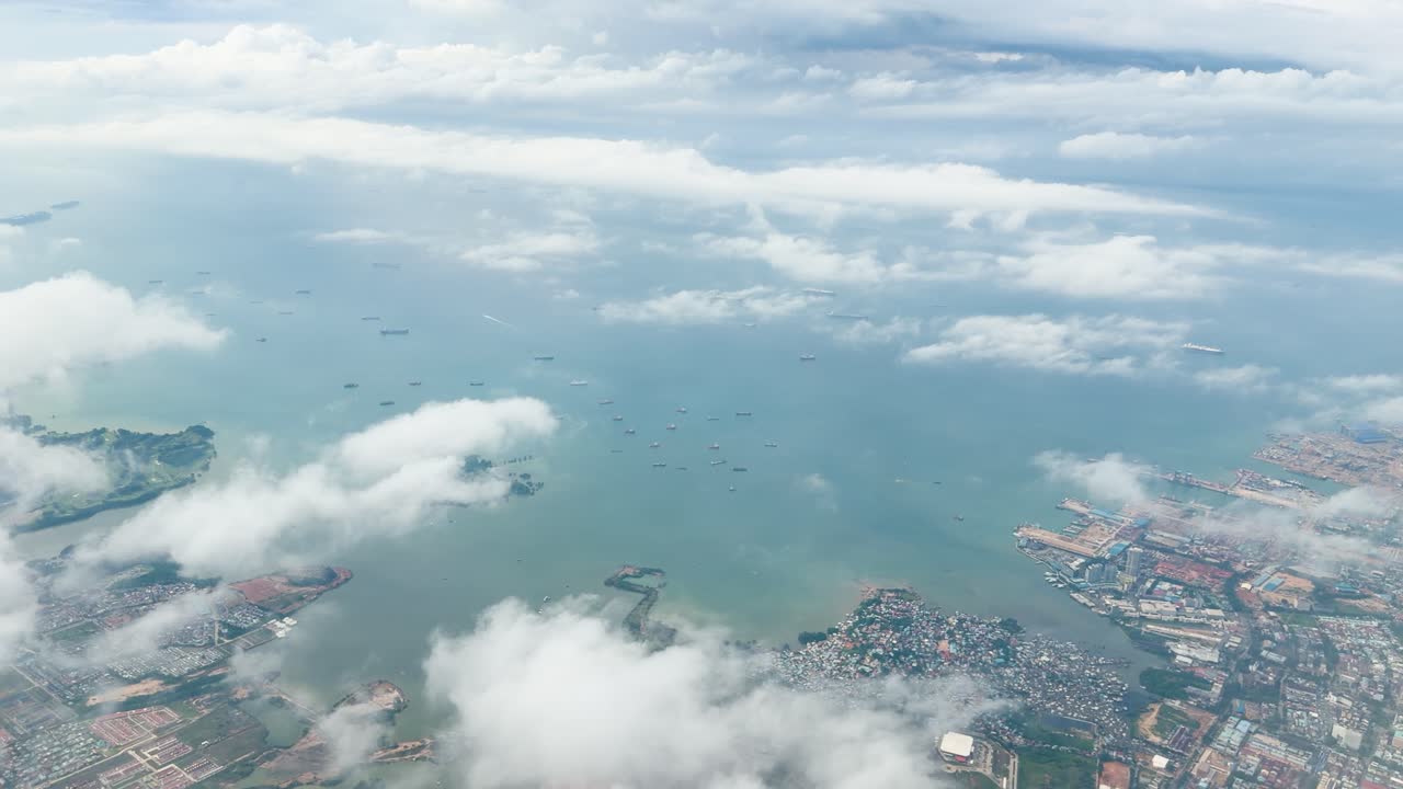 貨物船、沿岸部のコンテナ港、漂う雲、穏やかな日の光を捉えた、高高度からの航空機窓の眺め。