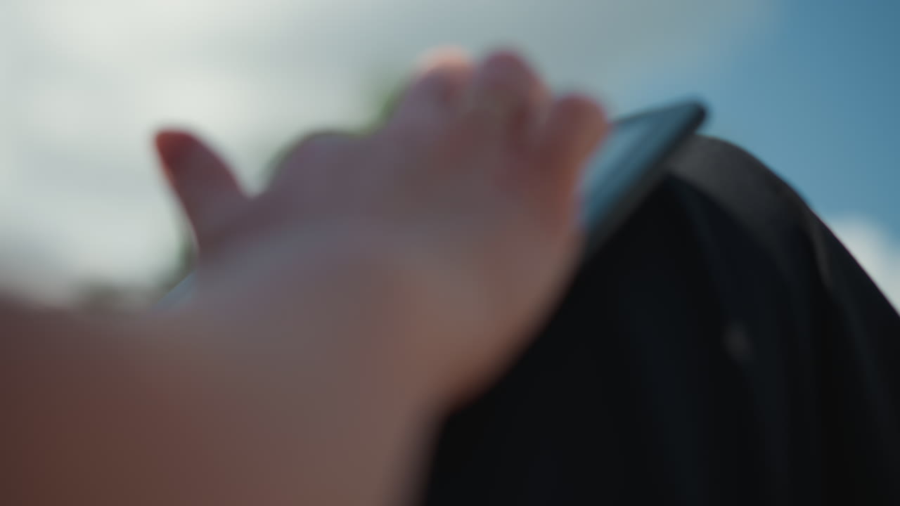 Close up side view of tech savvy person sliding through tablet outdoors under warm sunlight, showing motion blur and hand reflection, symbolizing focus, innovation
