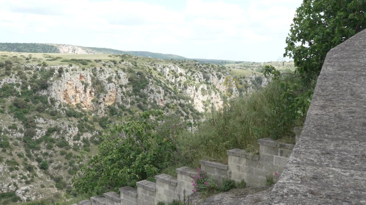 Una vista panorámica sobre un profundo desfiladero rocoso y escarpados acantilados naturales de piedra caliza desde el borde de un antiguo muro de piedra en la provincia de Matera, Italia.