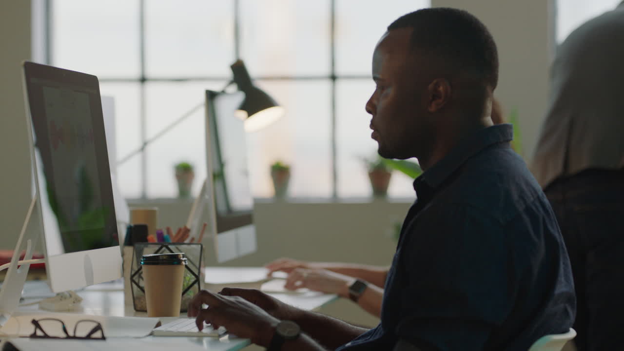 young african american businessman using computer typing developing creative design for company project in busy office background