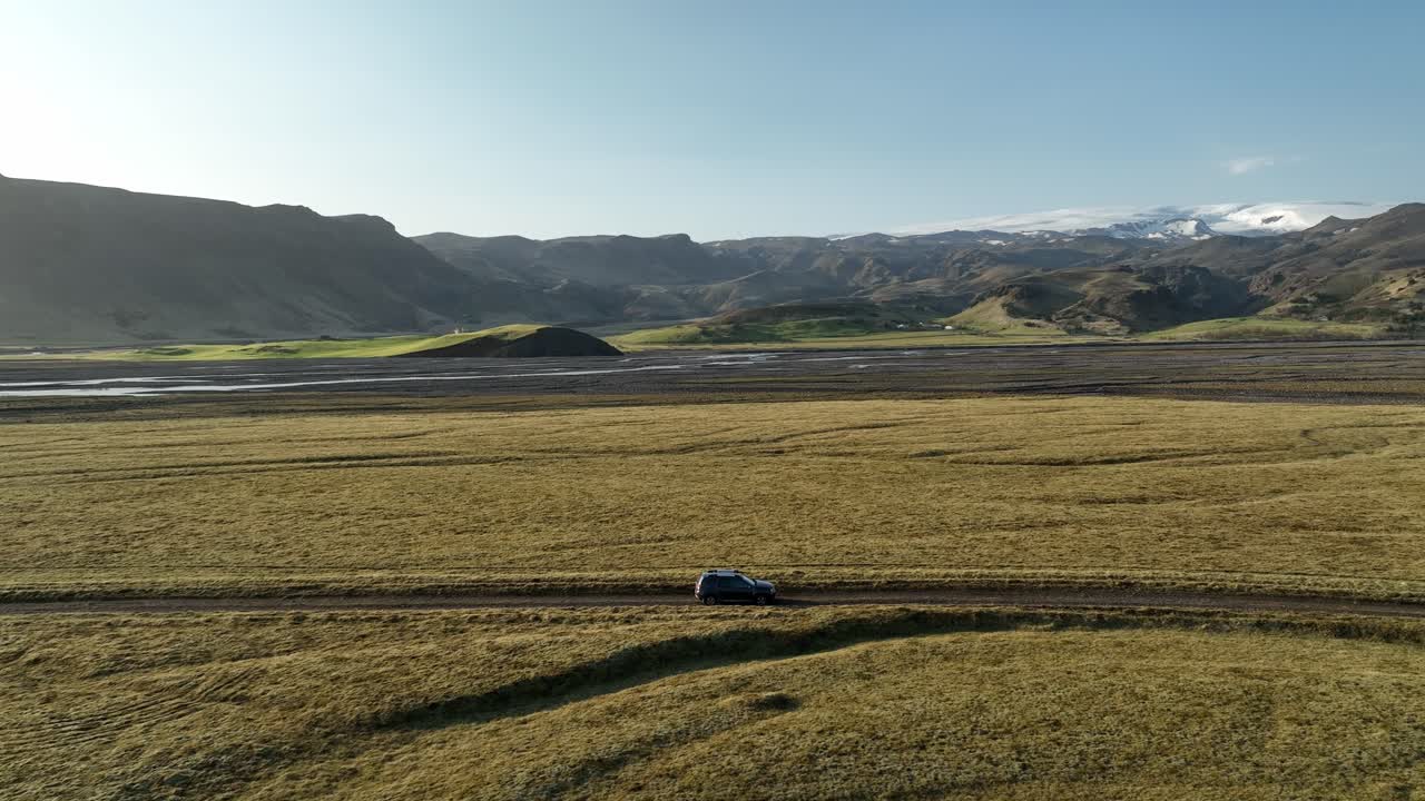 A 4x4 vehicle driving across the vast plains of North Iceland, with rugged mountains and glaciers in the background on a clear, sunny day.