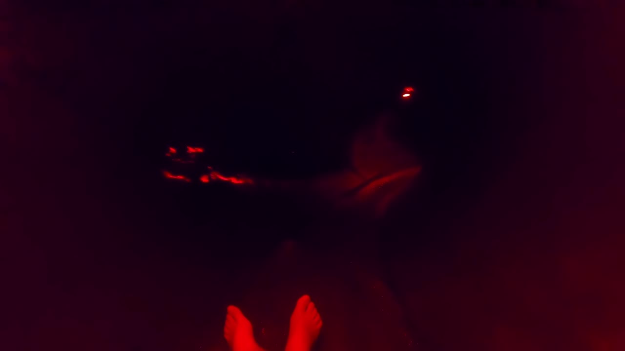 Primo piano POV giù per uno scivolo d'acqua buio, luce al neon rossa e blu, vista dei piedi.