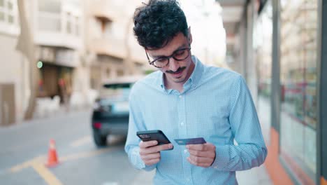 joven hispano usando teléfono inteligente y tarjeta de crédito en la calle