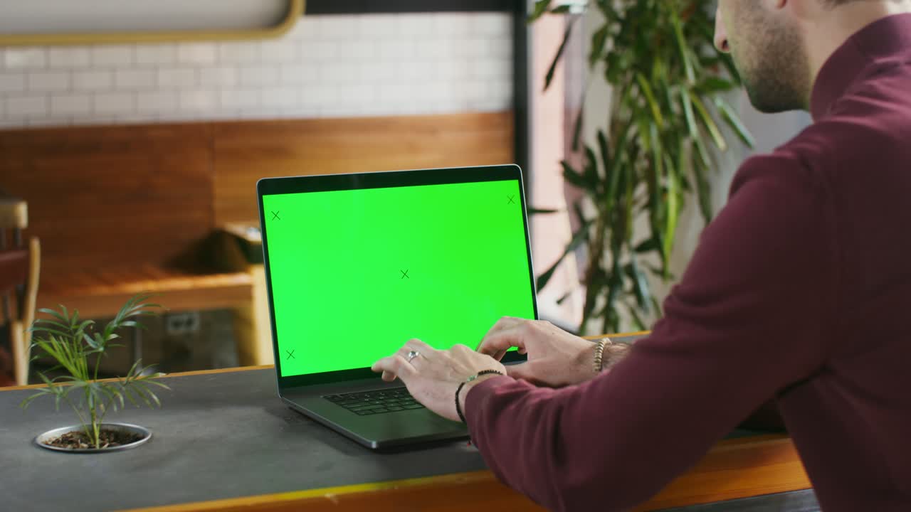hombre trabajando en una computadora portátil con pantalla verde en un café