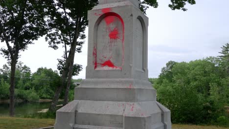 la cámara se inclina para revelar una estatua colonial de una mujer sosteniendo la cabeza de un nativo americano con pintura roja que representa la sangre