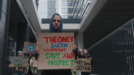 young male activist holding a cardboard placard during a climate change protest while looking at camera surrounded by others activists 1