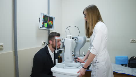 handsome man checking his eyes in clinic. young female doctor checking eyesight of a patient with a modern ophthalmology machine.