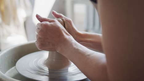 female potter shapes piece of clay on the pottery wheel.