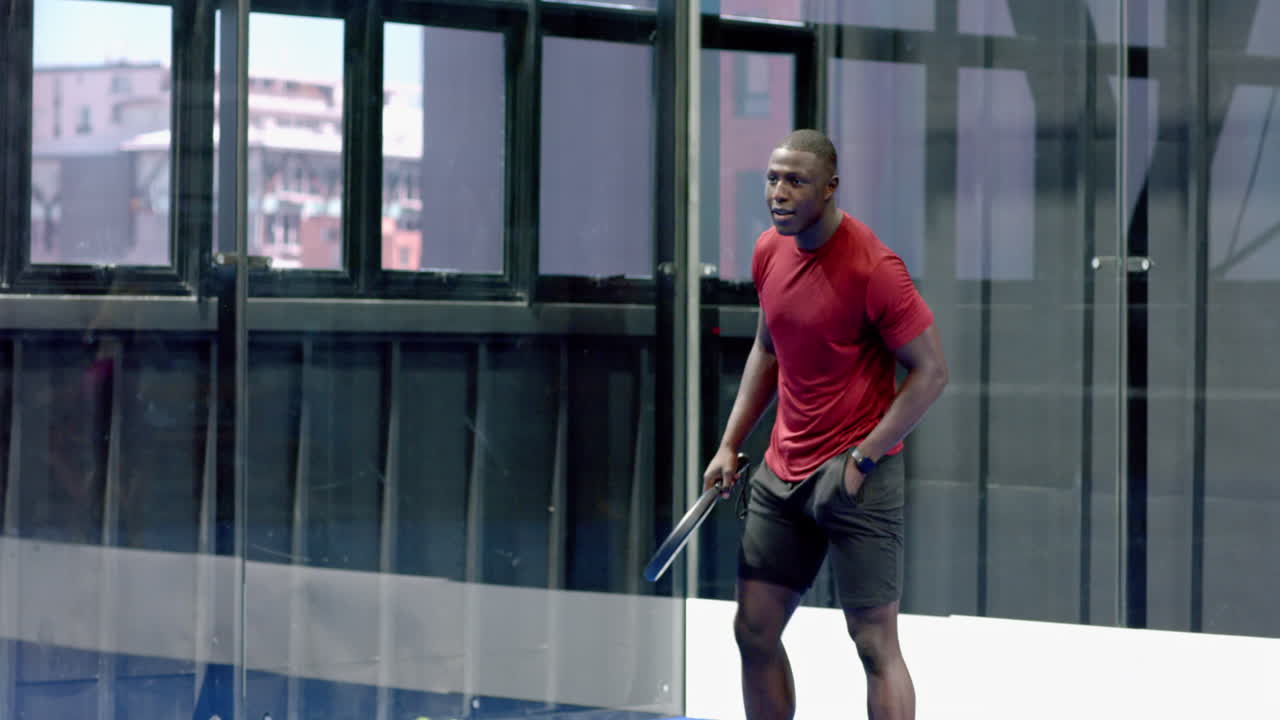 Athletic man playing padel tennis, focusing on hitting ball in urban indoor court