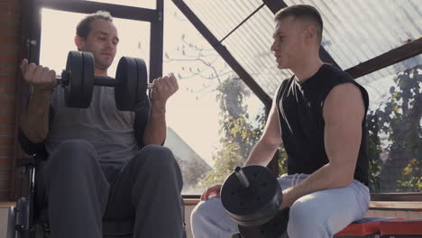 disabled man in wheelchair and his personal trainer working out with dumbbell at home 1