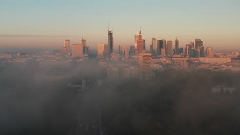 Forwards-fly-above-fog.-Panoramic-footage-of-downtown-high-rise-buildings-in-morning-sun-light.-Revealing-cityscape.-Warsaw,-Poland