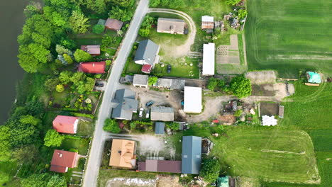 Aerial-view-of-a-small-village-in-Poland-with-houses,-some-with-red-roofs,-and-various-buildings-surrounded-by-greenery