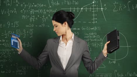 Woman-holding-calculator-and-notebook-standing-and-looking-around-in-front-of-chalkboard