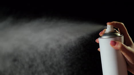 hand with a spray can sprays it on a black background