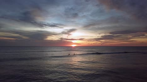 Drone-shot-of-waves-and-surfers-in-Aruba,-Caribbean-with-spectacular-sunset