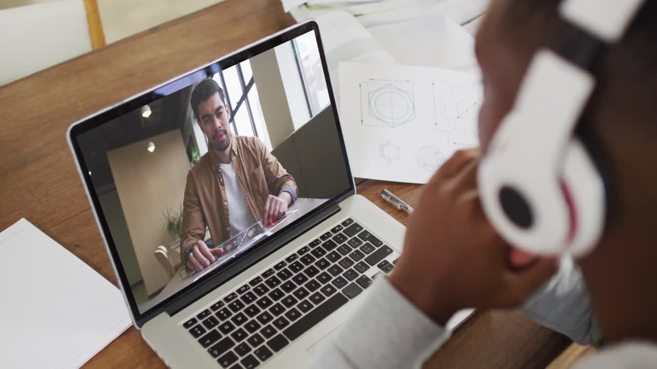 African american businessman sitting at desk using laptop having video call with male colleague