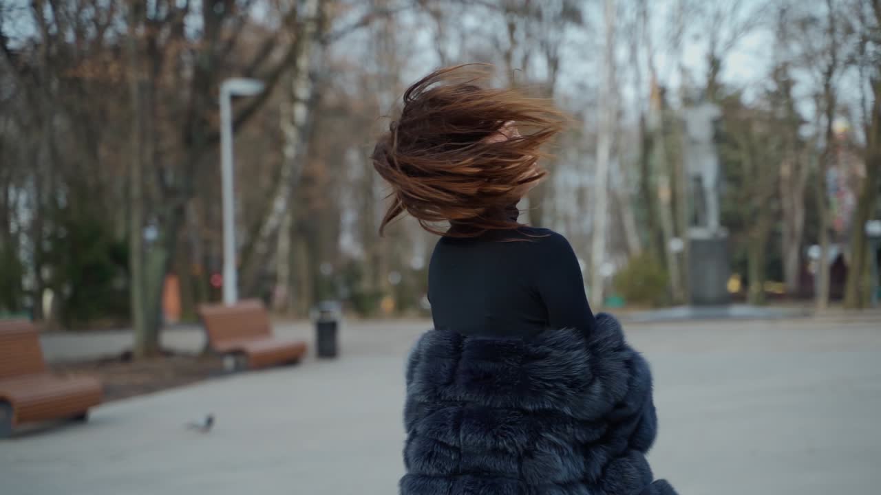 Fashionable girl with long hair looking at camera outdoors. Portrait of attractive young woman in fur coat poses on camera on the park background.