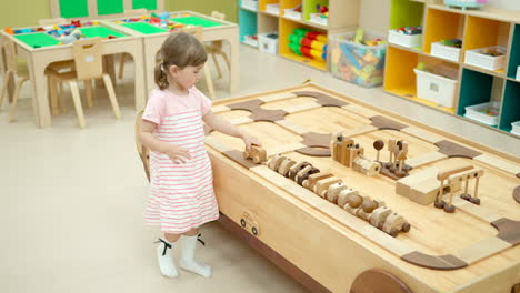 adorable 3-year-old girl toddler playing with wooden cars in modern playroom