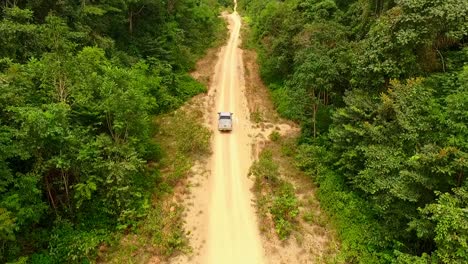 drone follows a pick up truck travelling down a dirt road in the amazon rainforest