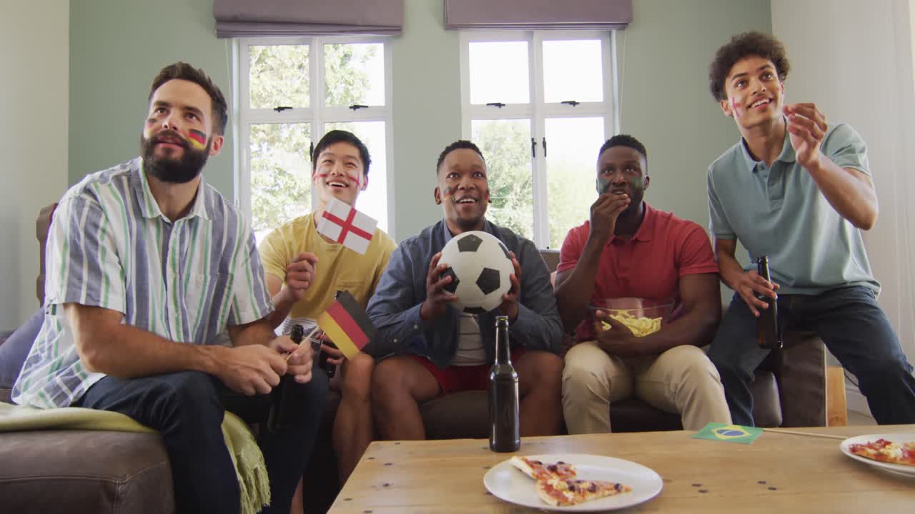 felices amigos varones diversos viendo televisión y bebiendo cerveza en la sala de estar