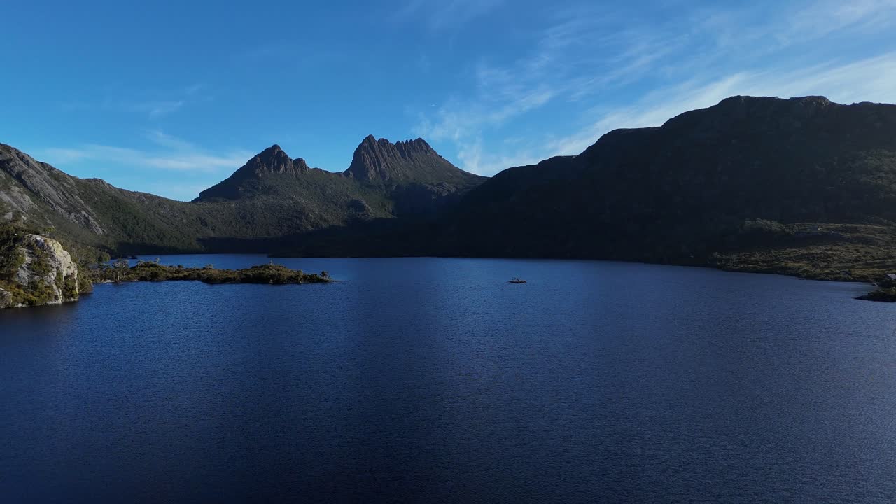 Aerial flight over tranquil Dove Lake and cradle mountains against blue sky. Beautiful calm landscape of national park in Tasmania, Australia. Wide shot.