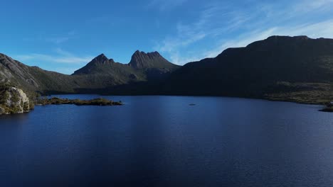 aerial flight over tranquil dove lake and cradle mountains against blue sky. beautiful calm landscape of national park in tasmania, australia. wide shot.