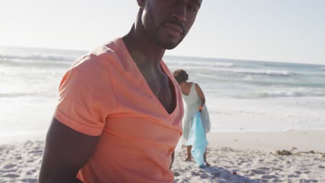 Portrait-of-african-american-couple-segregating-waste-with-gloves-on-sunny-beach